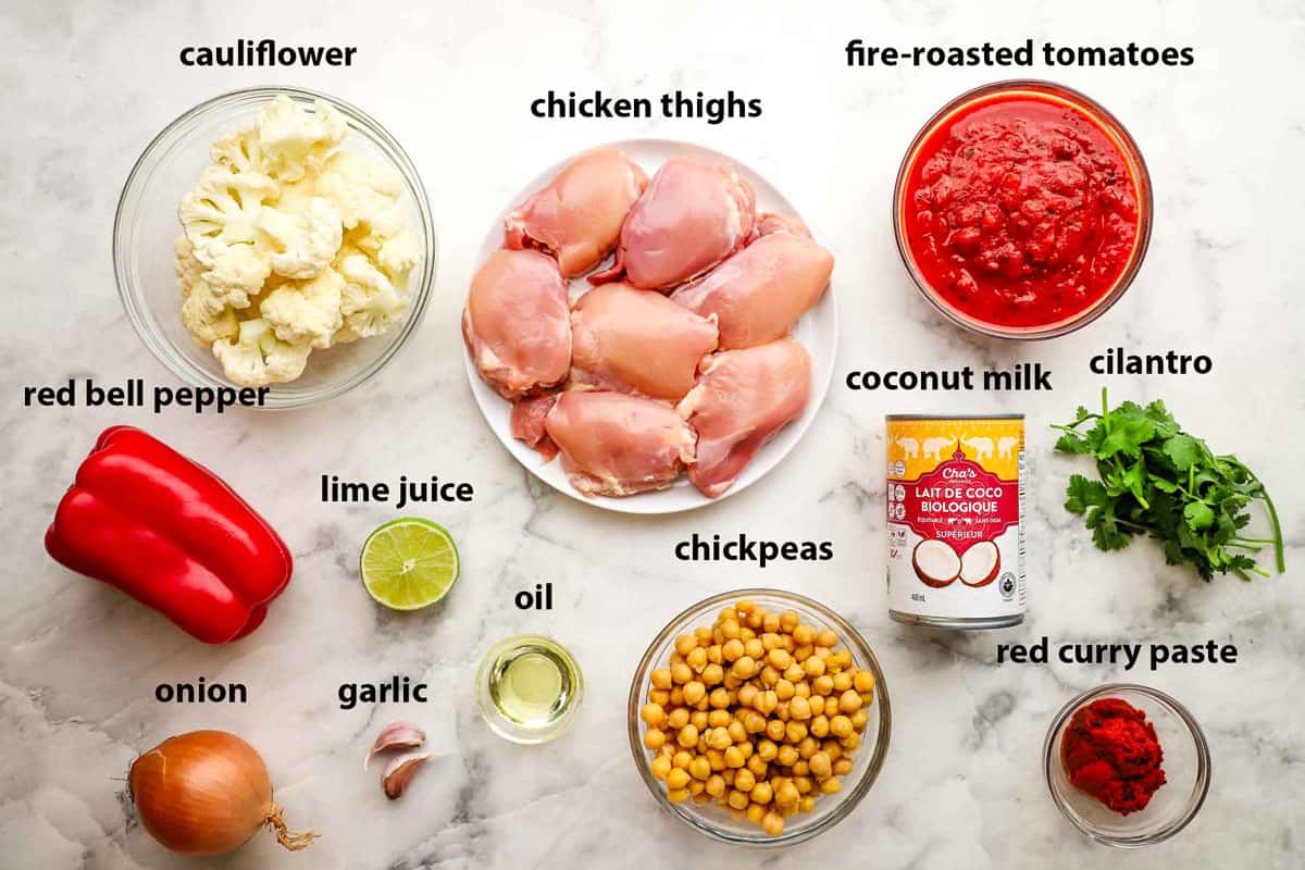 Top-down view of ingredients in bowls for chicken and chickpea curry that includes chicken thighs, cauliflower, lime juice, red curry paste, and coconut milk.