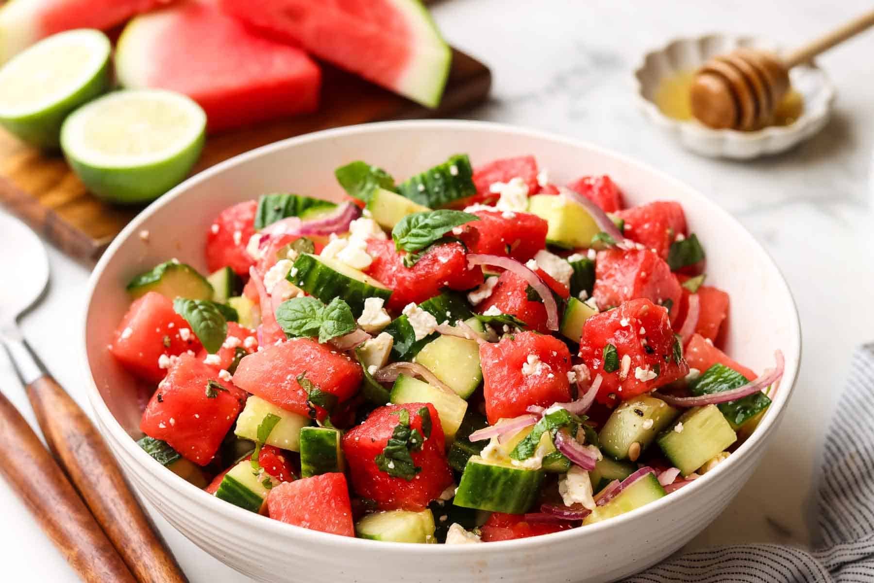 A bowl of cucumber watermelon salad with serving utensils.