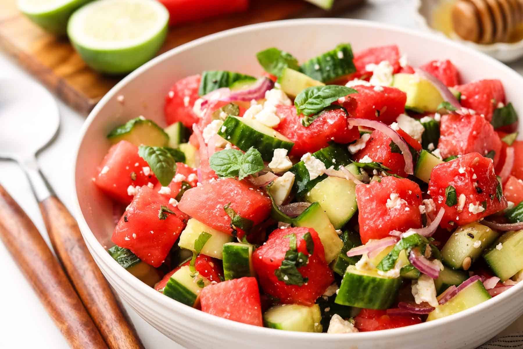 A bowl of cucumber watermelon salad with serving utensils.