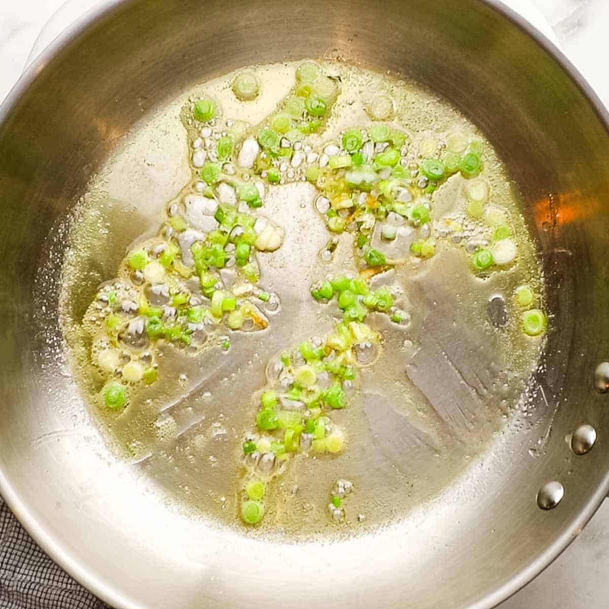 Scallion whites cooking in butter on a hot skillet. 