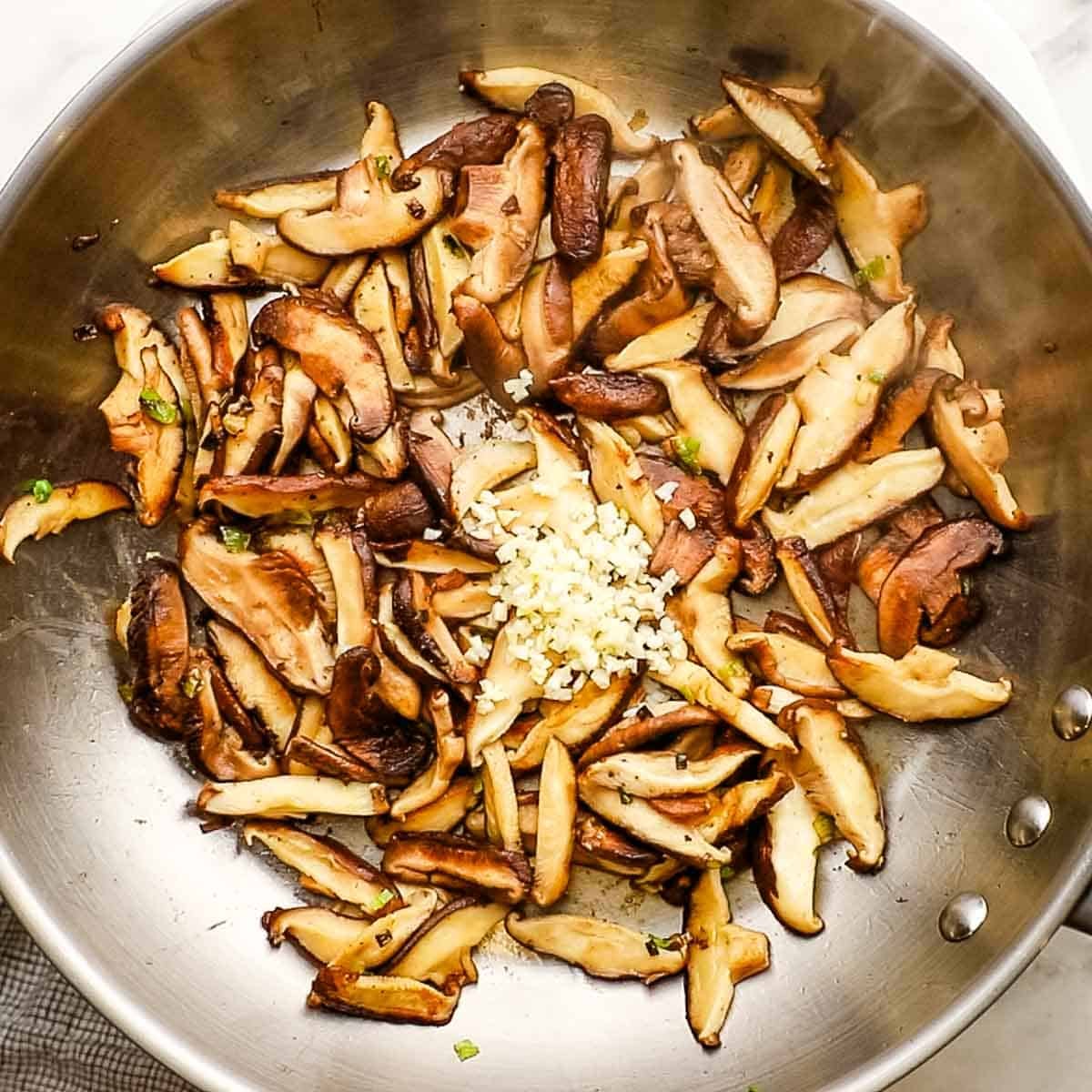 Shiitake mushrooms sliced and garlic added to a skillet with the scallions.