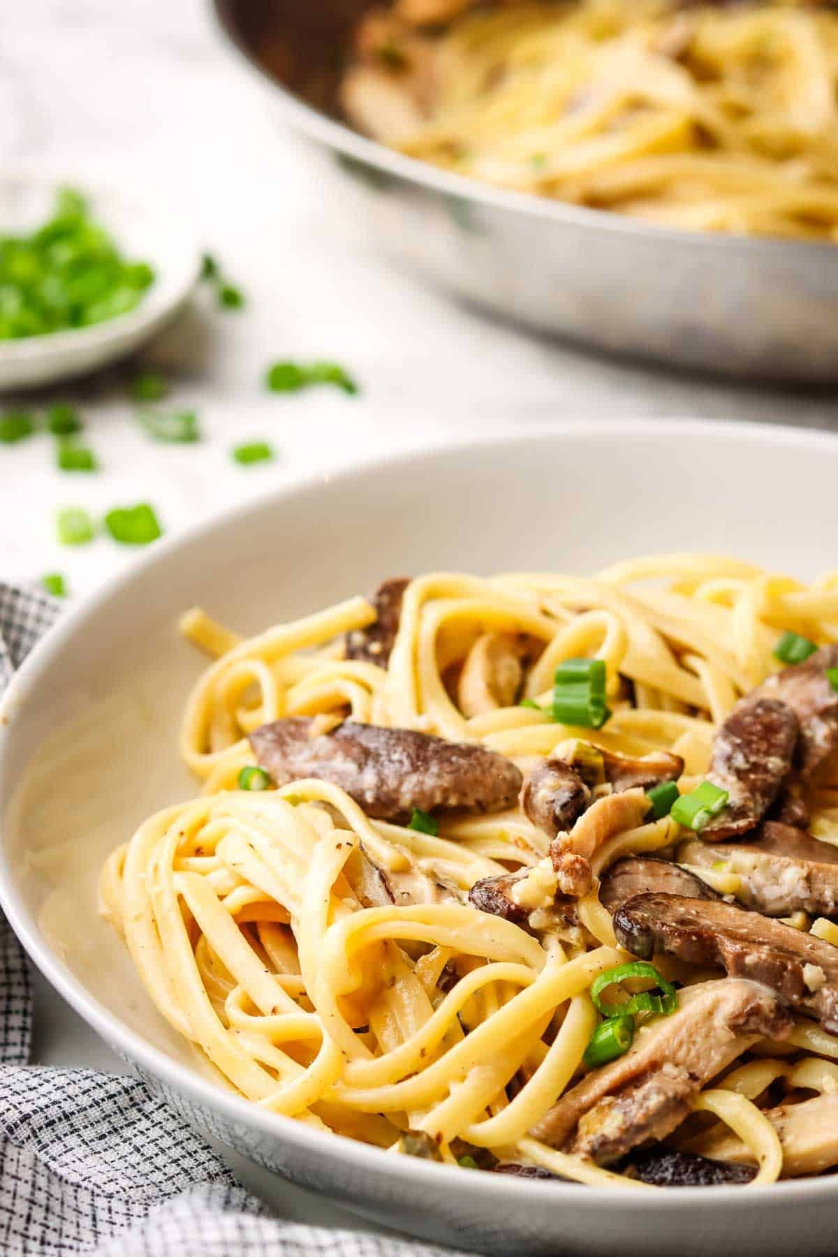 A serving bowl of miso mushroom pasta garnished with scallions.