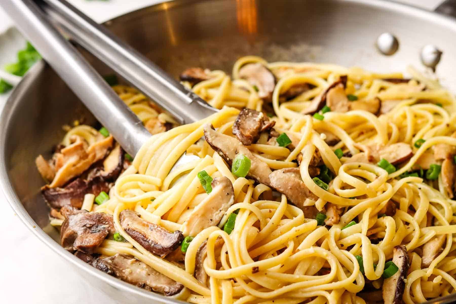 A skillet of miso mushroom spatula with noodles wrapped around tongs for serving.
