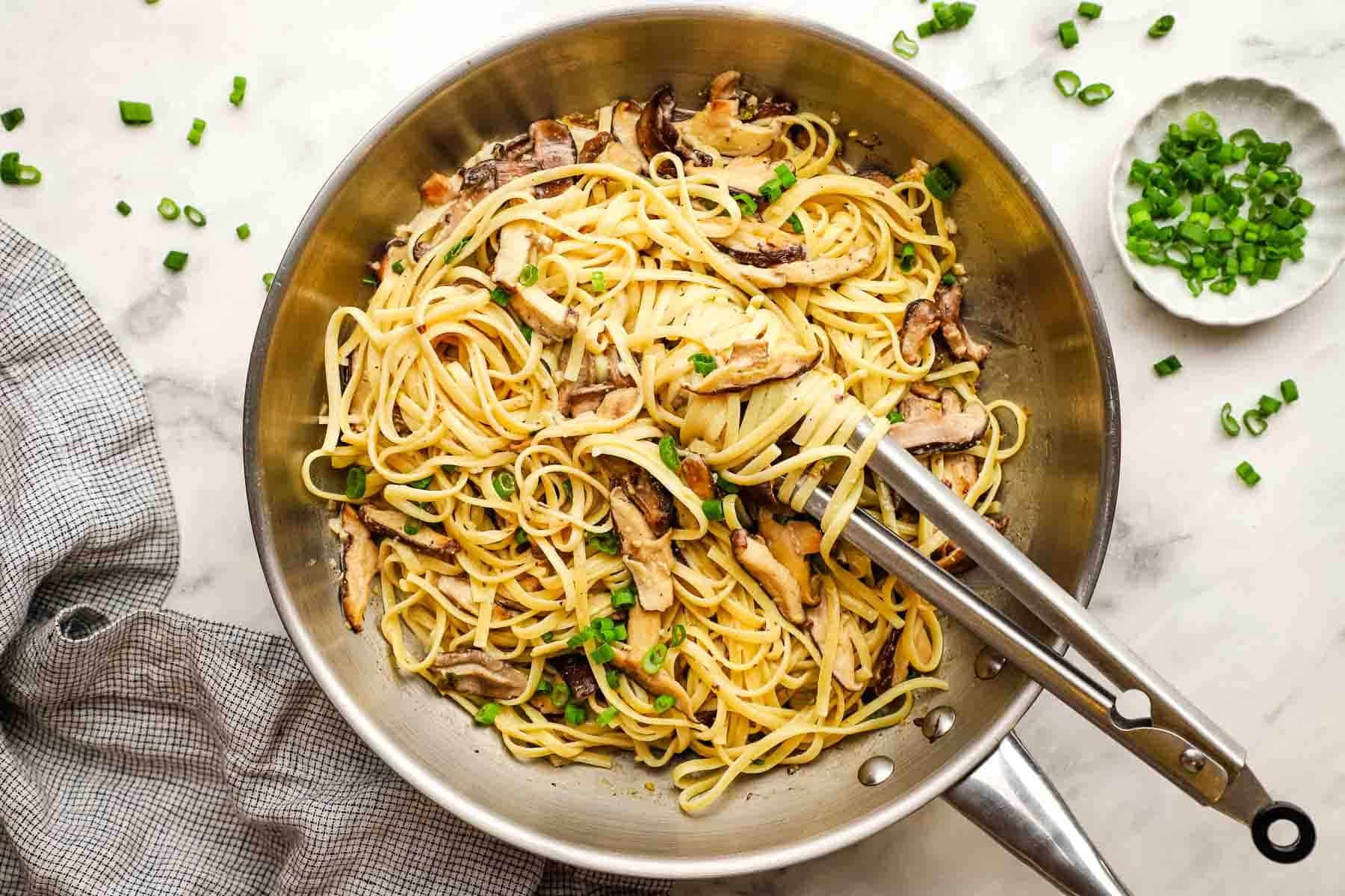 Miso Mushroom Pasta ready to be served with tongs, gently stirring and preparing to dollop on a plate.