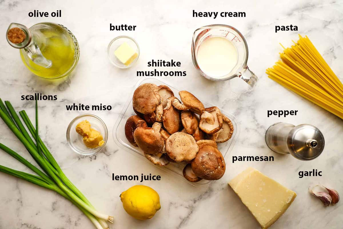 Top-down view of ingredients in bowls and plates for miso mushroom pasta that include shiitake mushrooms, butter, heavy cream, pepper, avocado oil, miso paste and more.