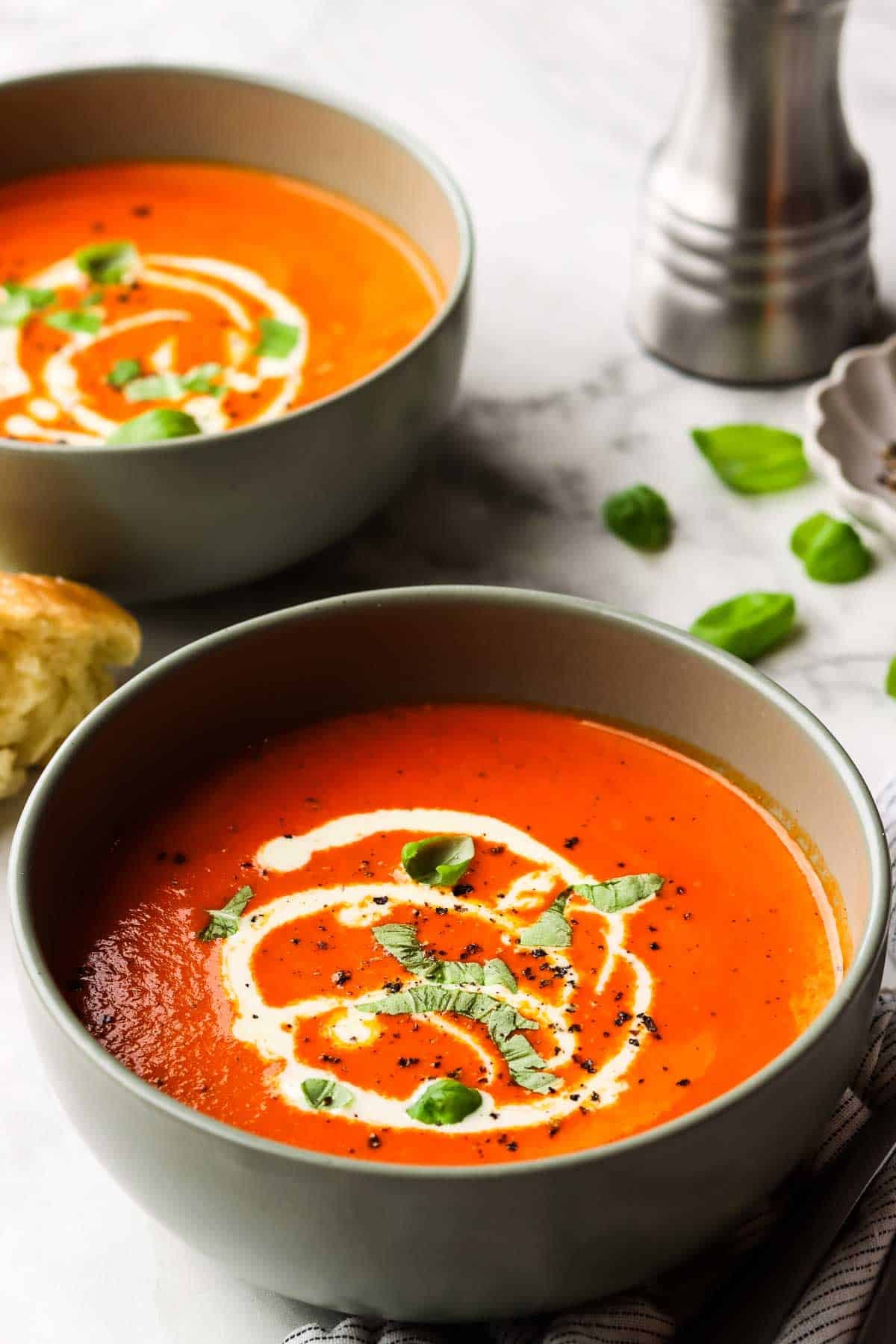 Two bowls of roasted red pepper soup garnished with a drizzle of cream and fresh basil.