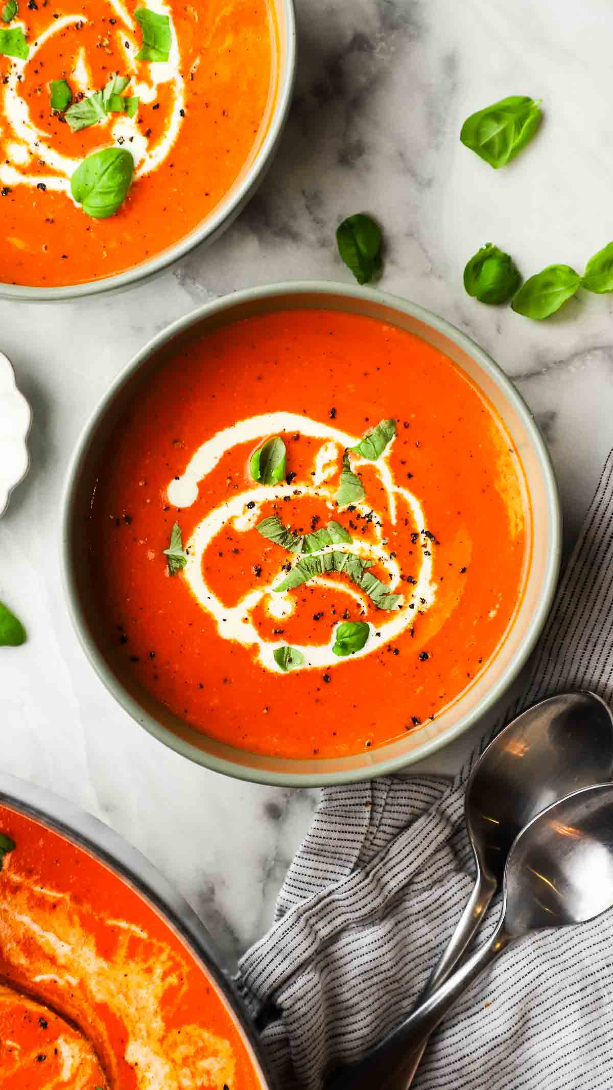 Top-down view of roasted red pepper and gouda soup topped with cream and basil and ground pepper.