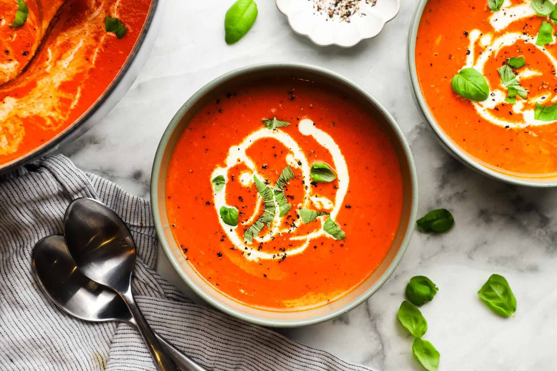 Bowls of creamy red pepper soup swirled with cream.