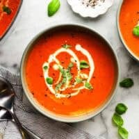 A bowl of roasted red pepper soup garnished with a drizzle of cream and fresh basil.