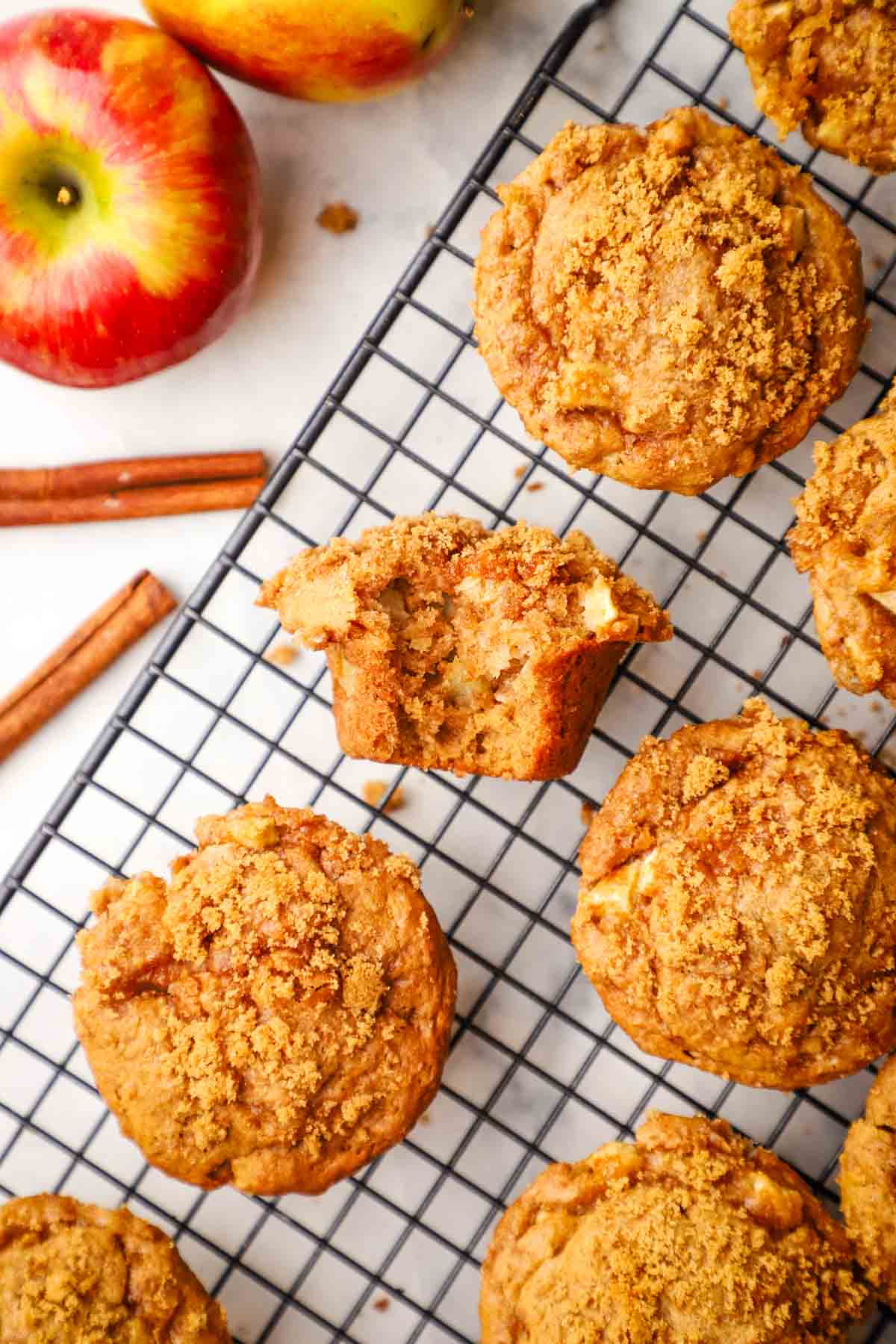 overhead view of apple sour cream muffins cooling on a wire rack with one muffin cut in half to show the inside.
