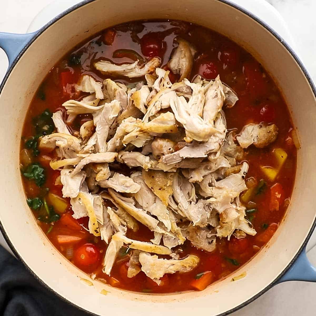 Shredded, precooked chicken added to the simmering pot of veggies and chicken stock for chicken orzo bake.