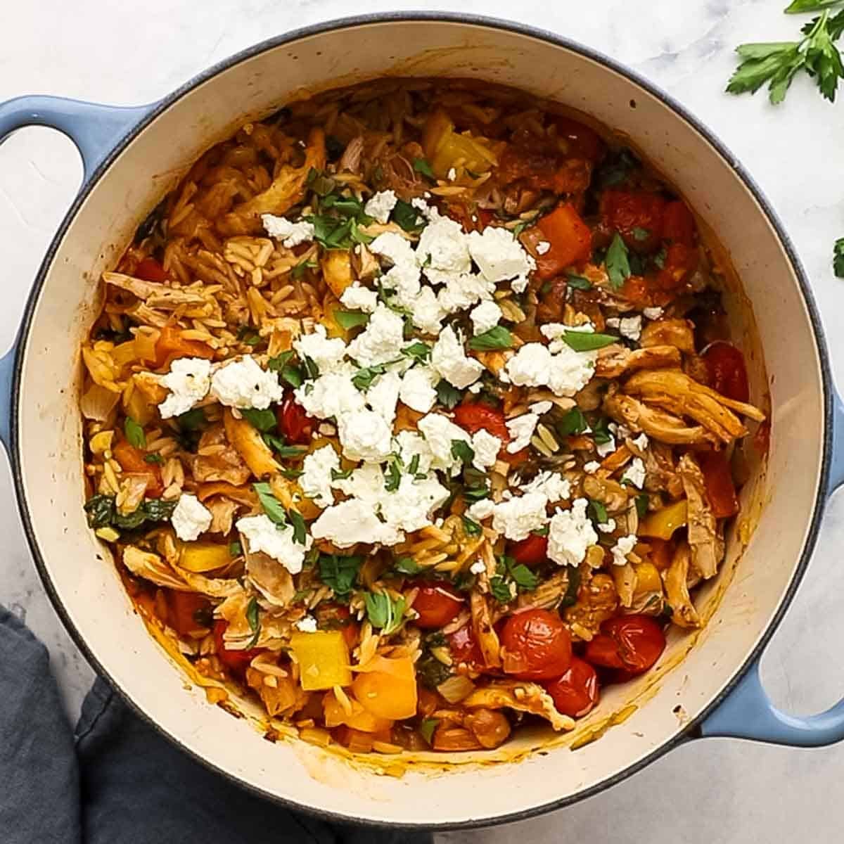 Top-down view of Mediterranean baked chicken and orzo in a Dutch oven topped with feta and parsley.