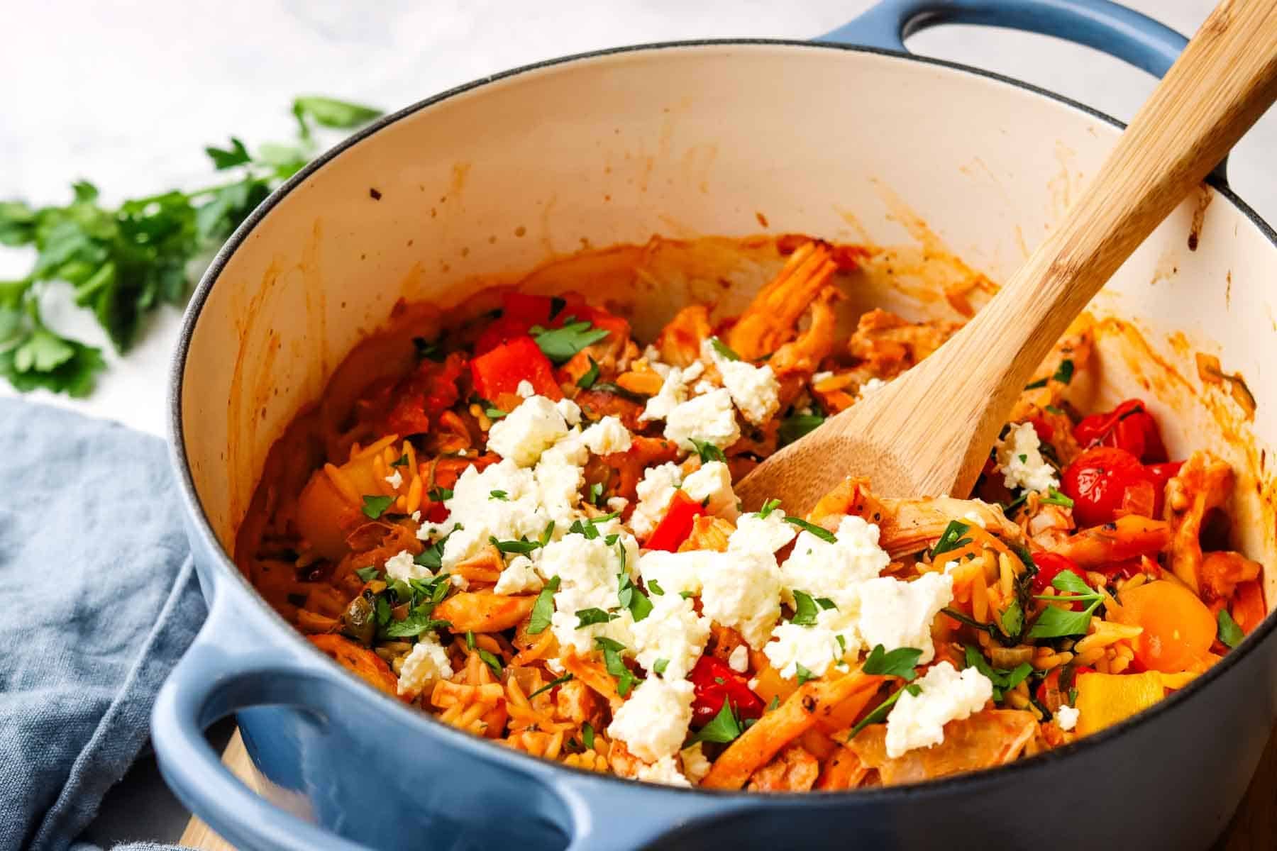 A pot of mediterranean chicken and orzo with a serving spoon.