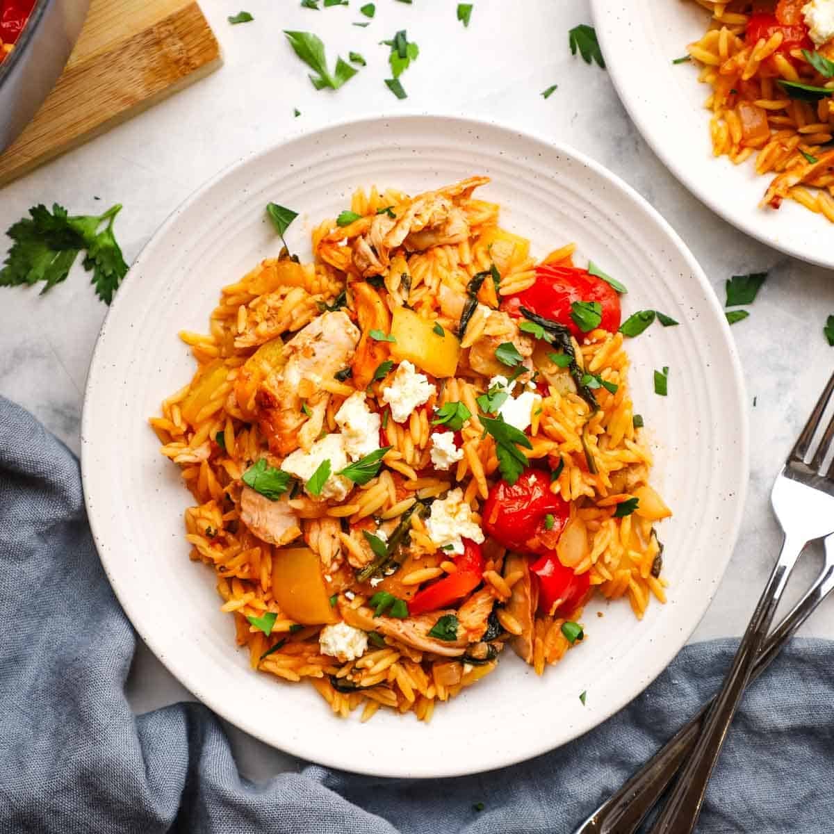 A plate of orzo pasta with vegetables garnished with feta and parsley.