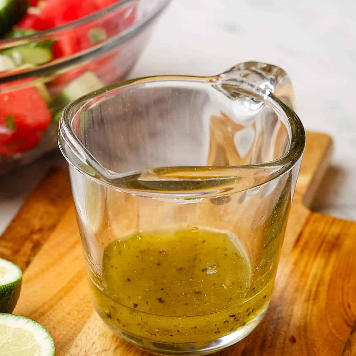 Dressing ingredients for watermelon and cucumber salad that include olive oil, honey, salt and pepper and more whisked in a glass container.