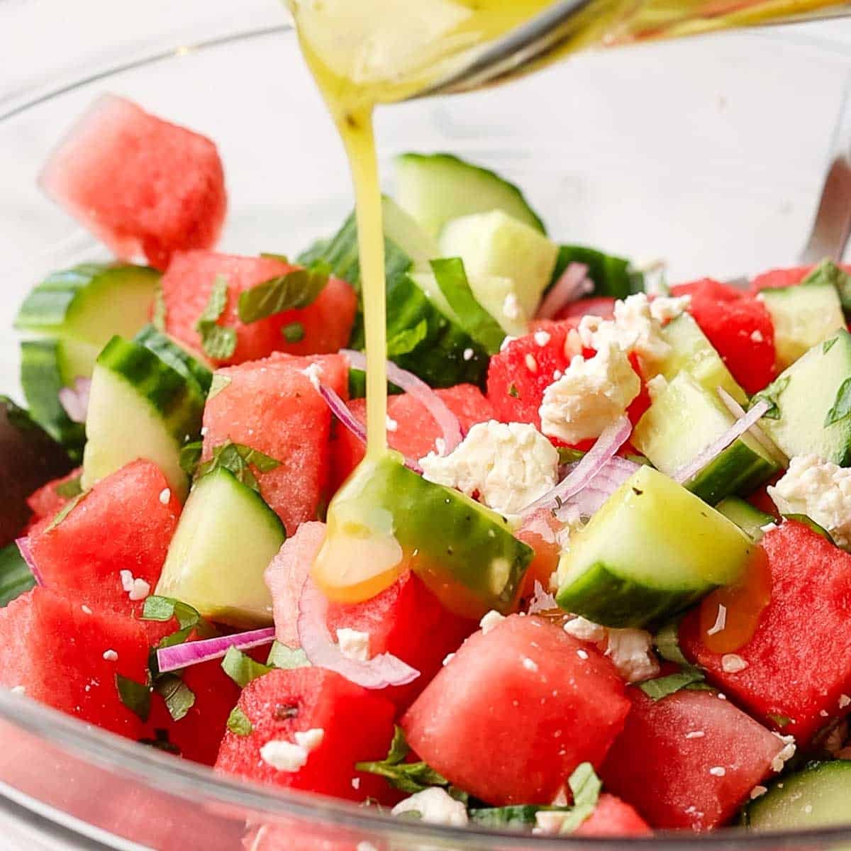 Dressing being added and then stirred gently into the watermelon cucumber salad.