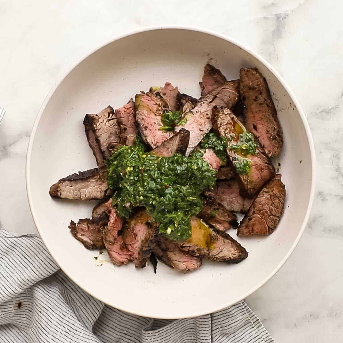 chimichurri added to the sliced steak in a bowl