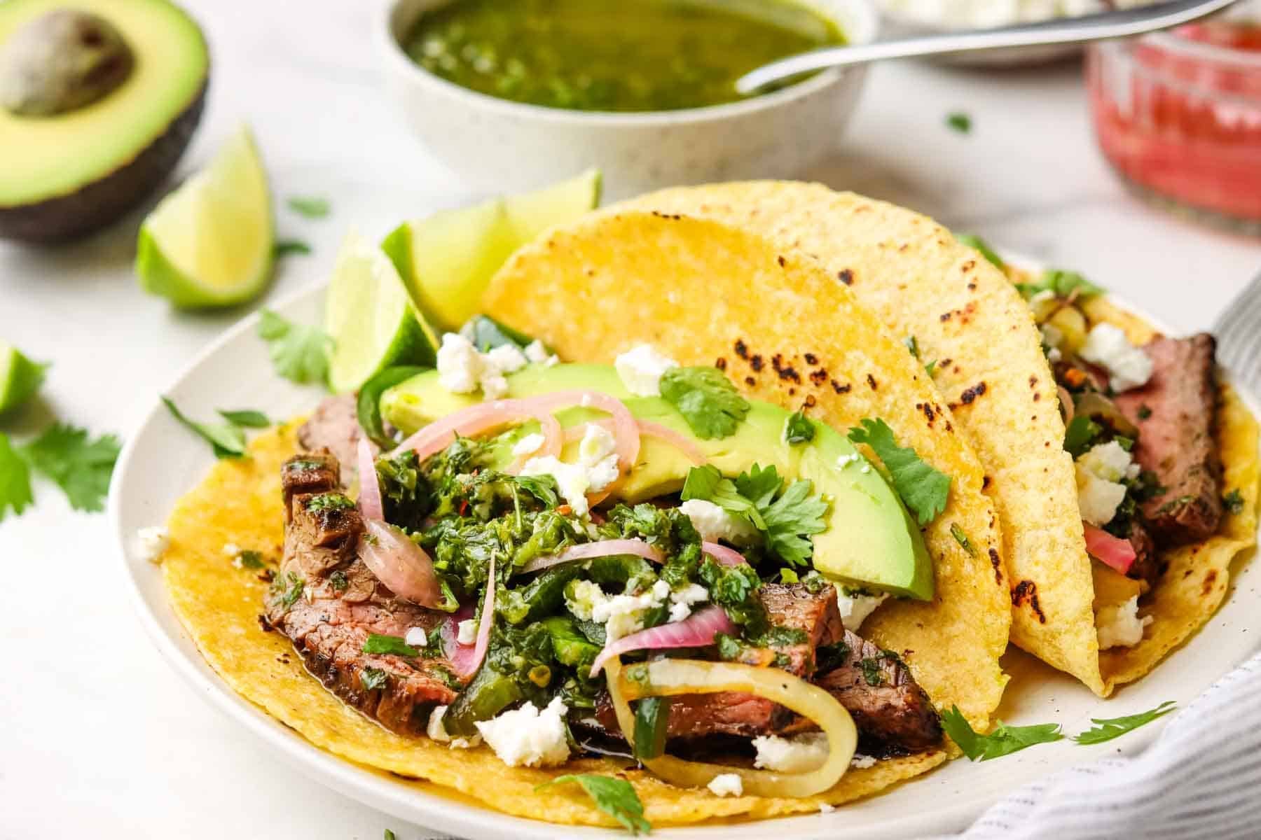 A steak taco with chimichurri with garnishes on a plate.