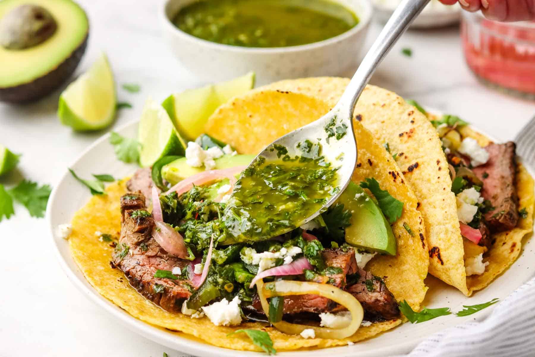 pouring chimichurri over steak tacos with a spoon