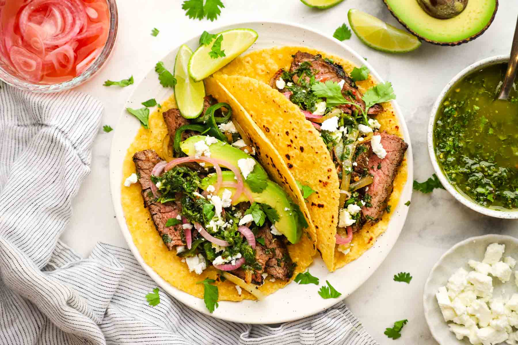overhead view of steak tacos with toppings and chimichurri