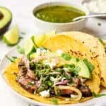 Two steak tacos with chimichurri and garnishes on a plate.