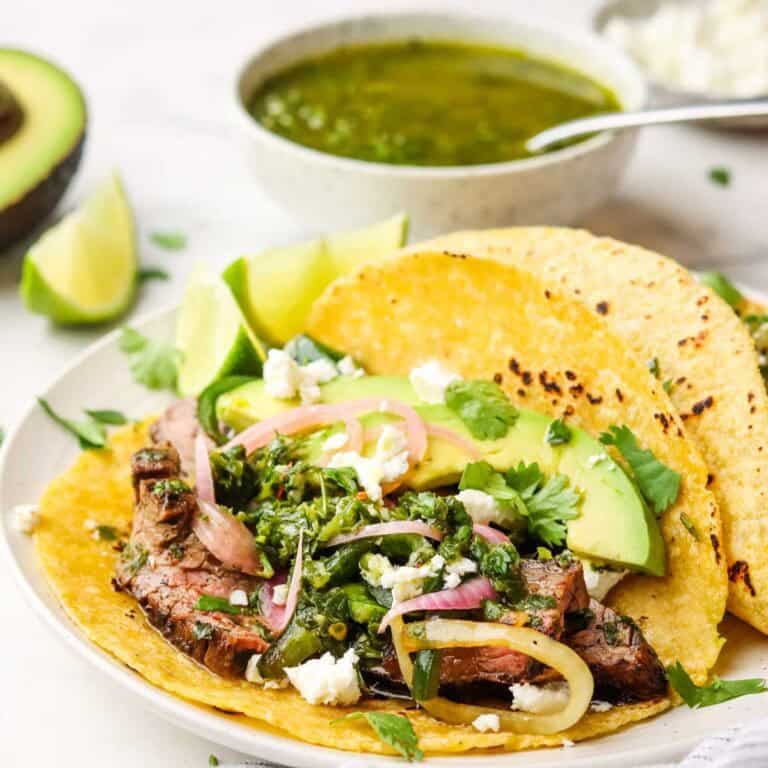 Two steak tacos with chimichurri and garnishes on a plate.