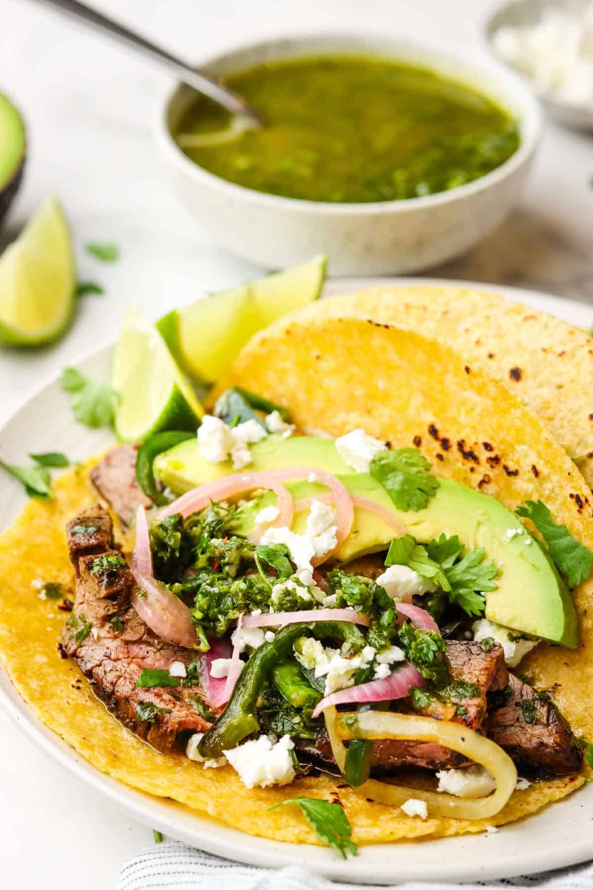 A steak taco with chimichurri with garnishes on a plate.