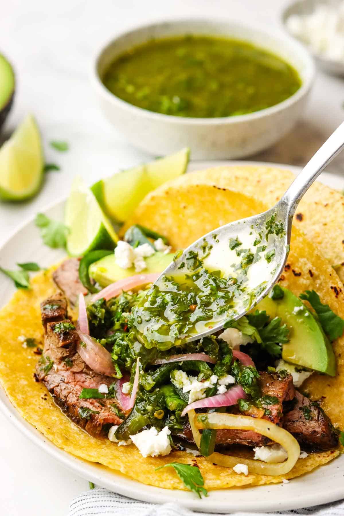 pouring chimichurri over steak tacos with a spoon