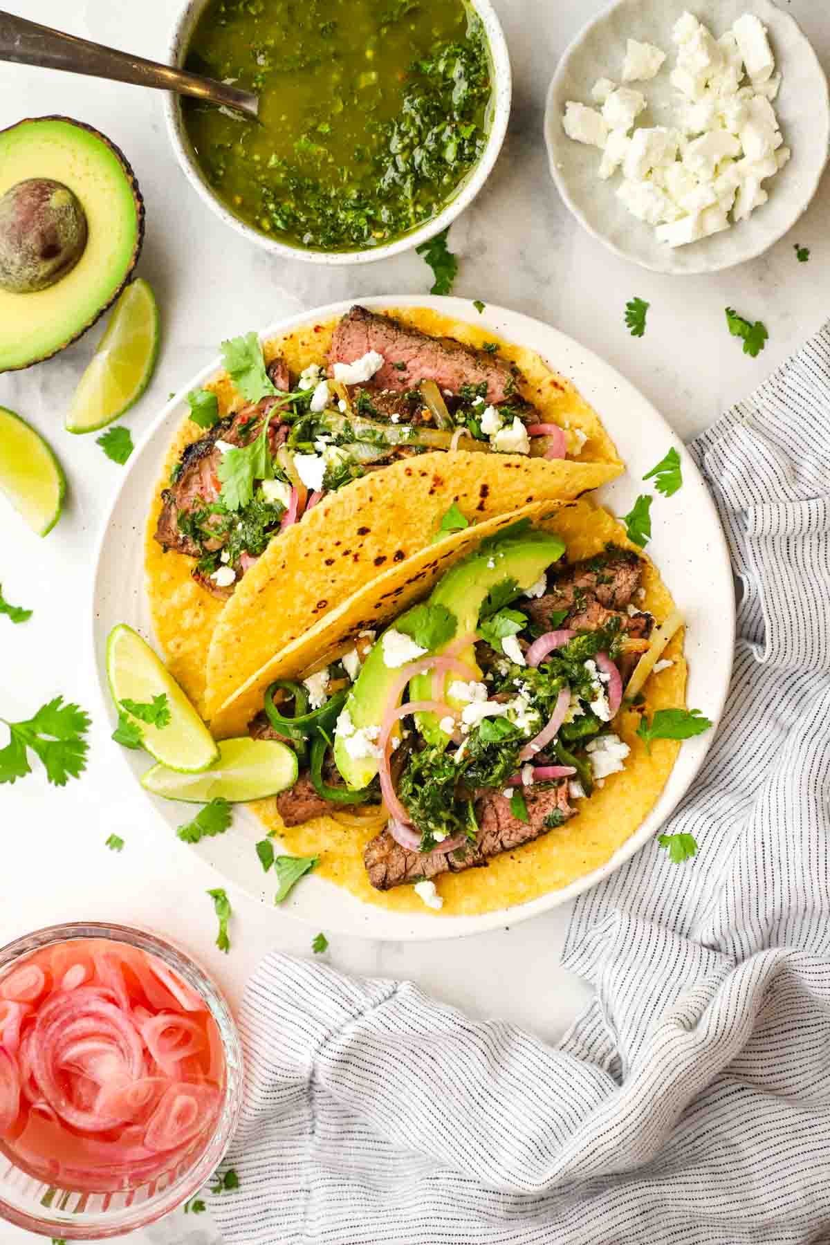 overhead view of steak tacos with toppings and chimichurri
