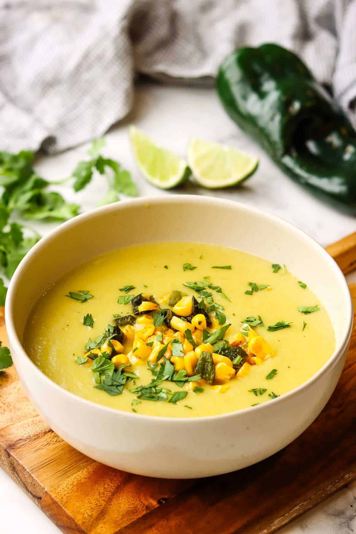 A bowl of creamy corn poblano potato soup on a wooden board.