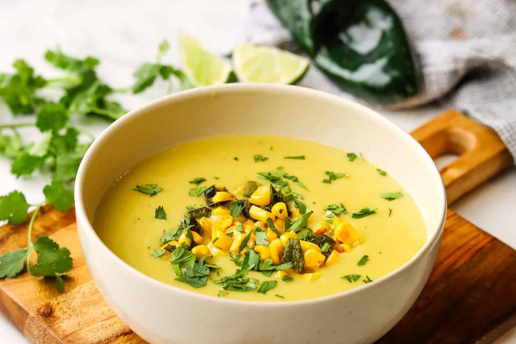 A bowl of creamy corn poblano potato soup on a wooden board.