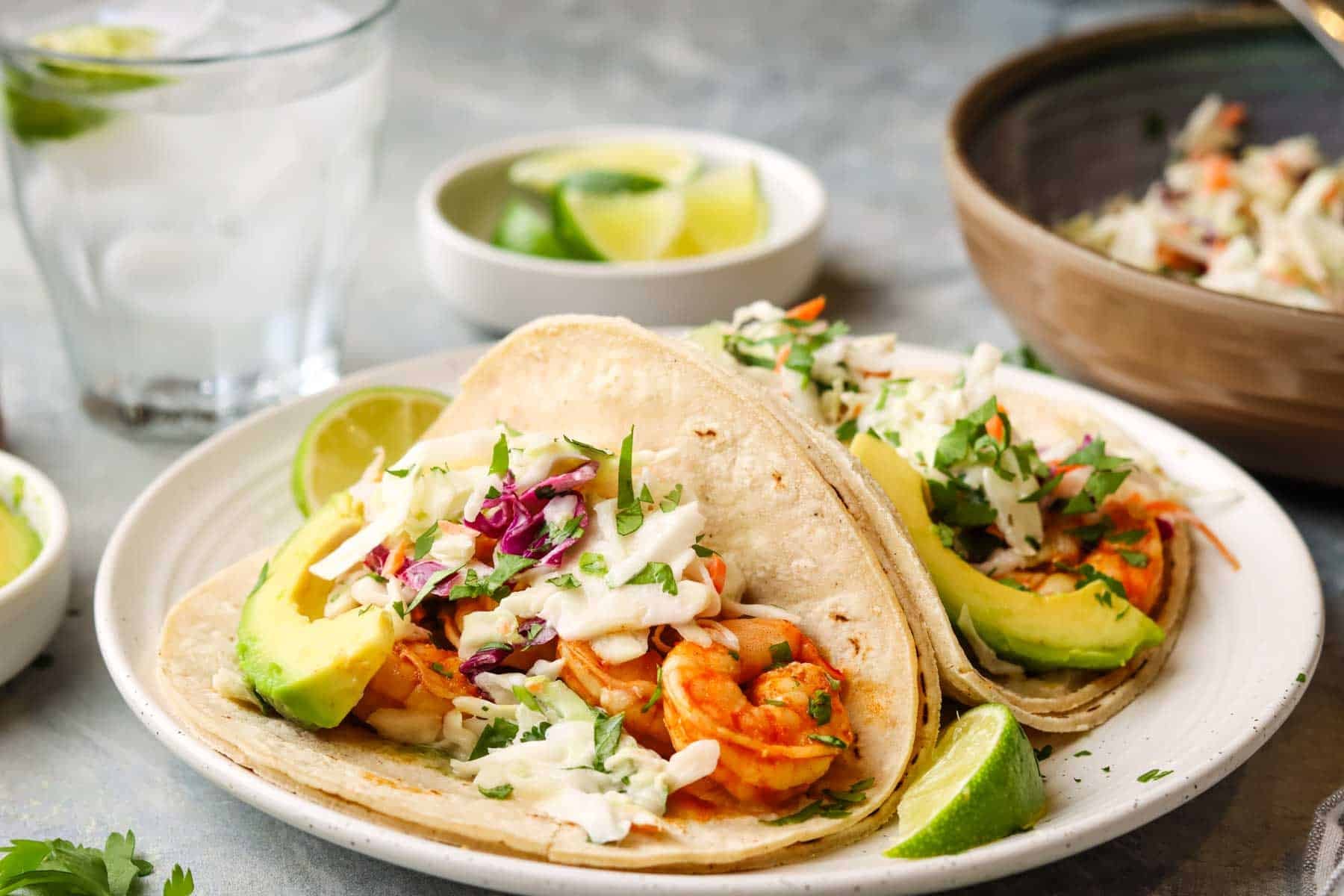 two tacos on a plate with shrimp and coleslaw in them.