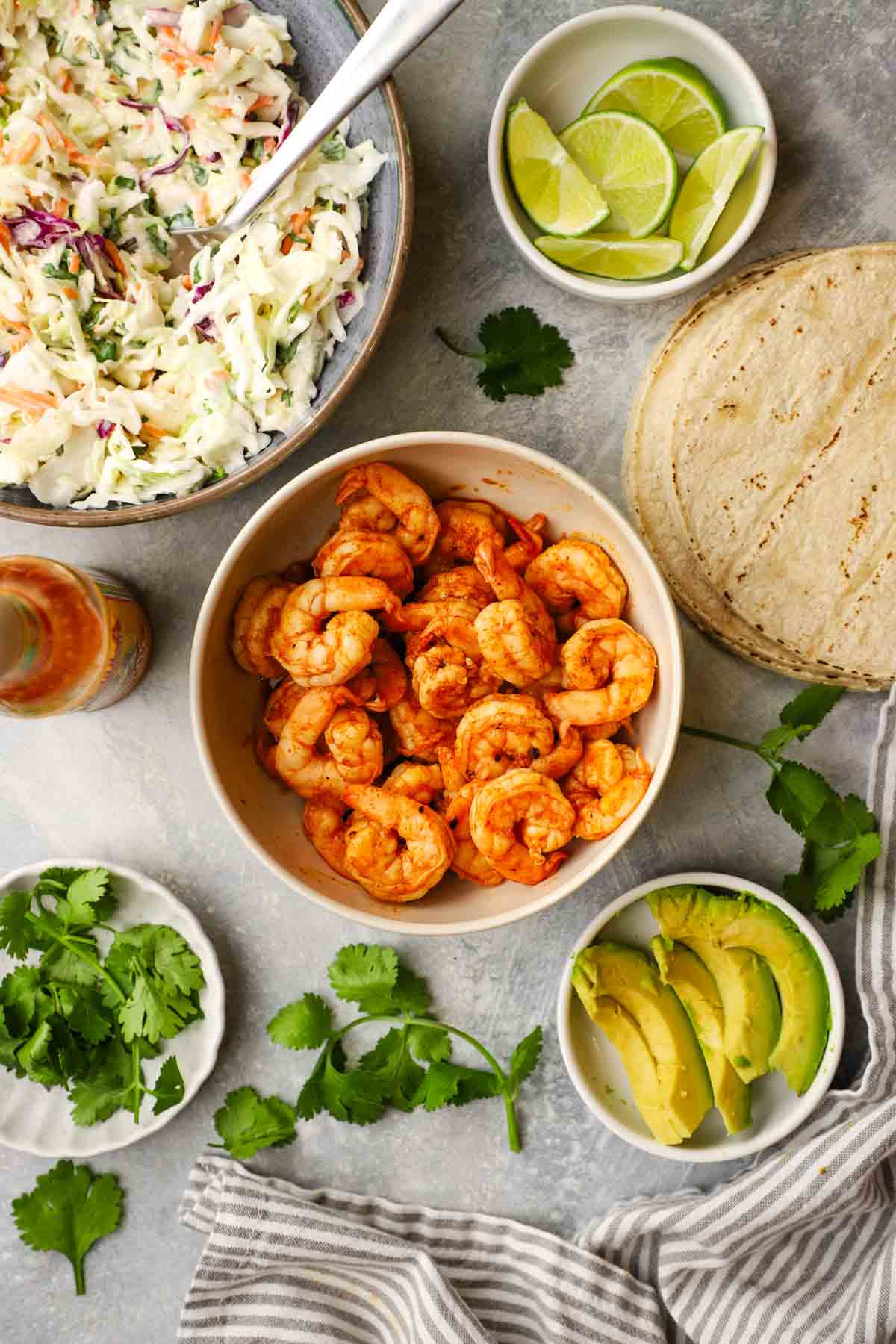 overhead view of a bowl of grilled shrimp, tortillas, coleslaw, and toppings.