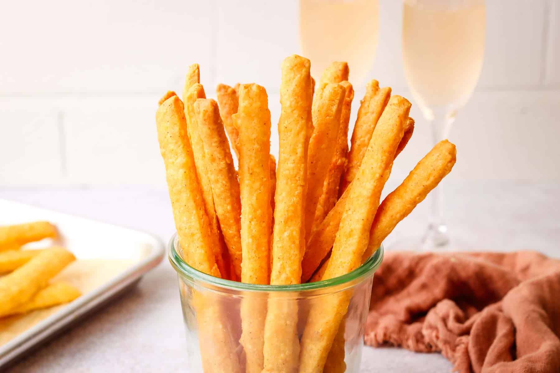 Cheese straws in a cup with champagne glasses in the background.