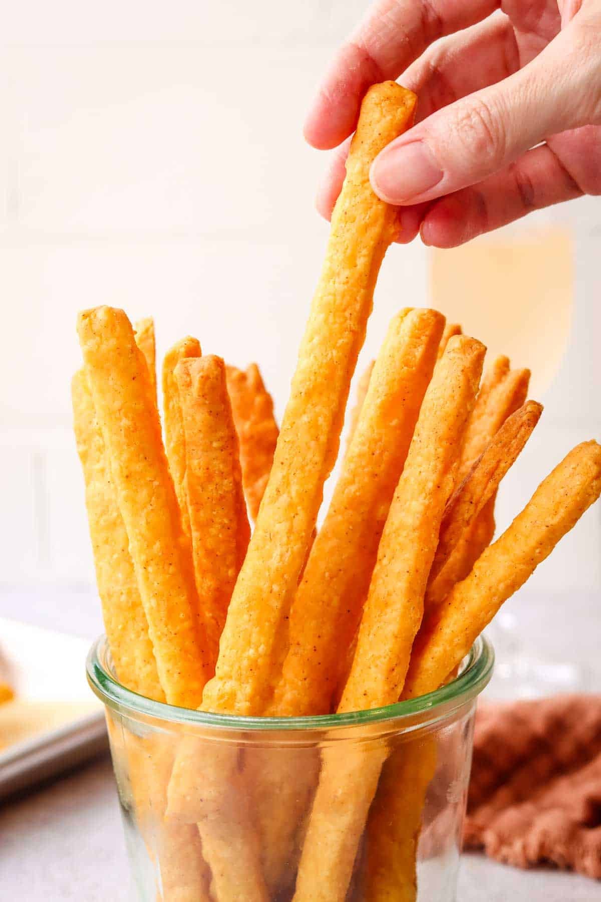 a hand picking out a cheese straw from a mason jar of cheese straws