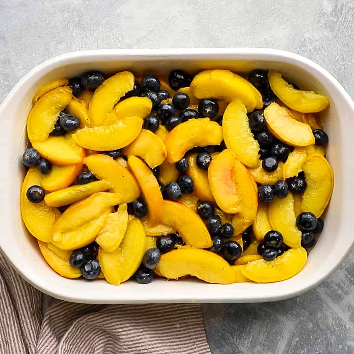 peach and blueberry filling spread in a baking dish,