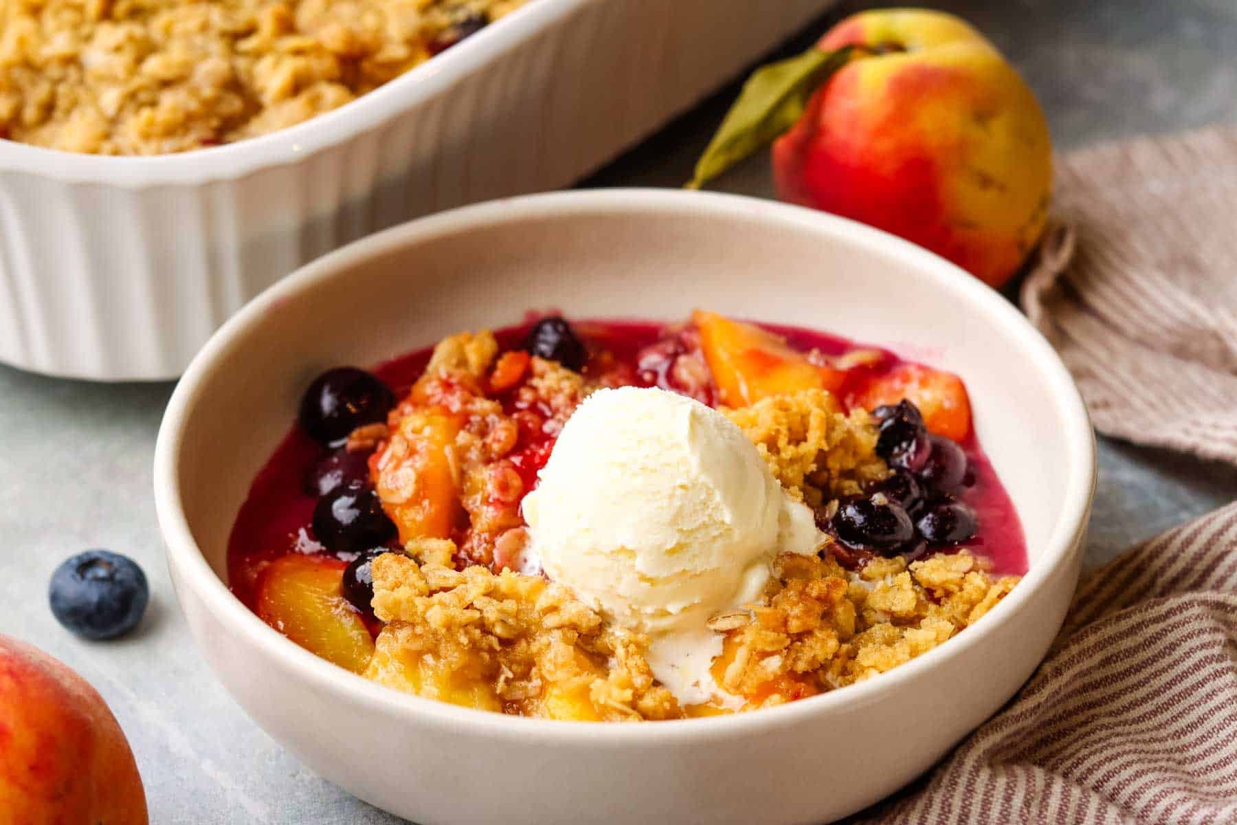 a bowl of peach blueberry crisp topped with vanilla ice cream.
