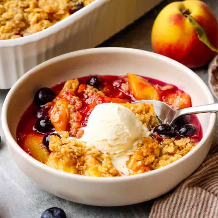 a bowl of peach blueberry crisp topped with vanilla ice cream.