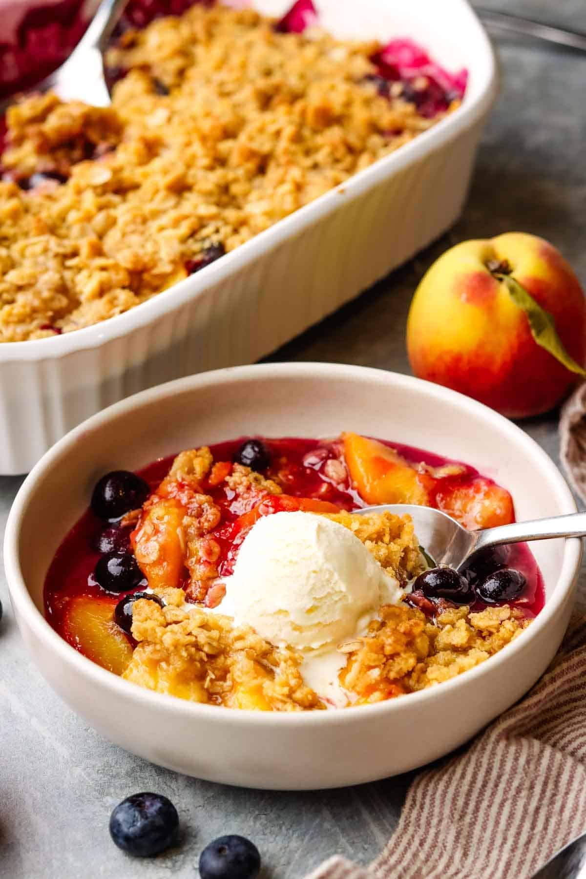 a bowl of peach blueberry crisp served with vanilla ice cream scoop.