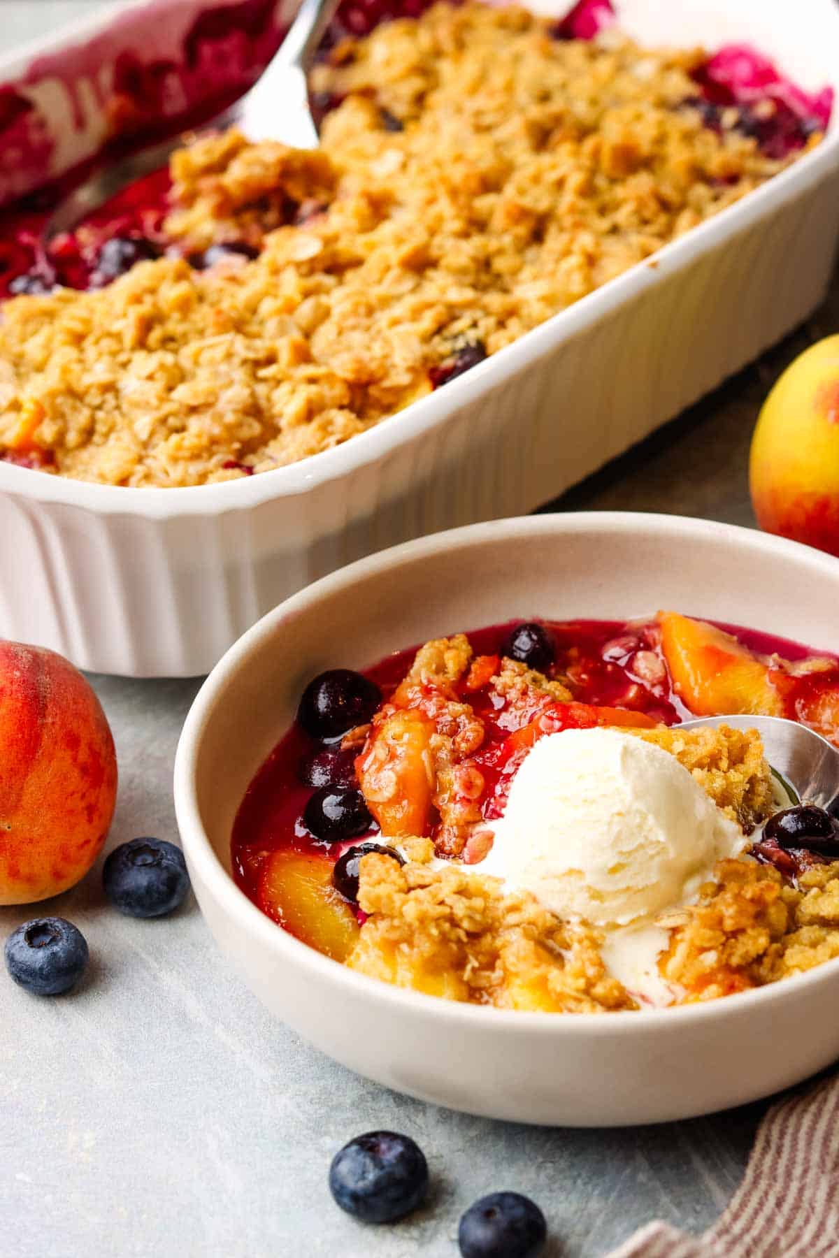 a bowl of peach blueberry crisp served with vanilla ice cream scoop.