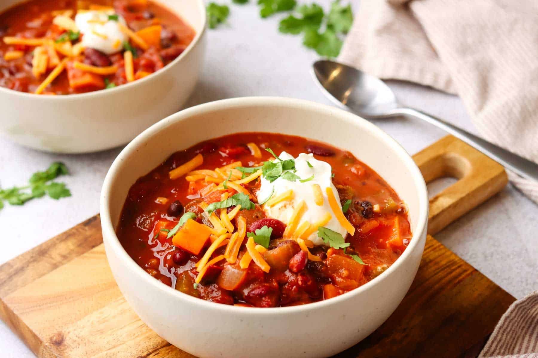 a bowl of sweet potato chili with sour cream, shredded cheese as toppings