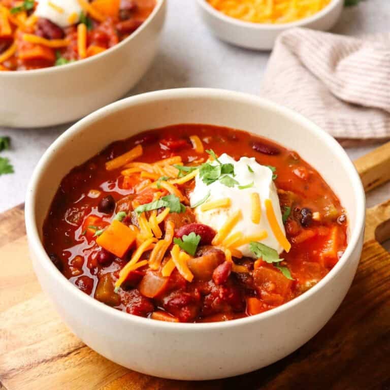a bowl of sweet potato chili topped with shredded cheese and sour cream