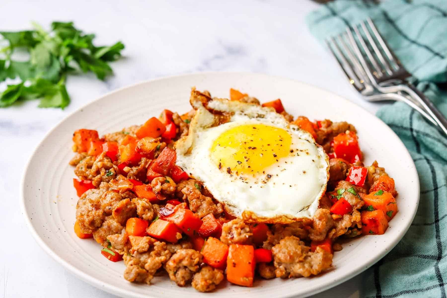 a plate of sweet potato and sausage hash, topped with a fried egg.