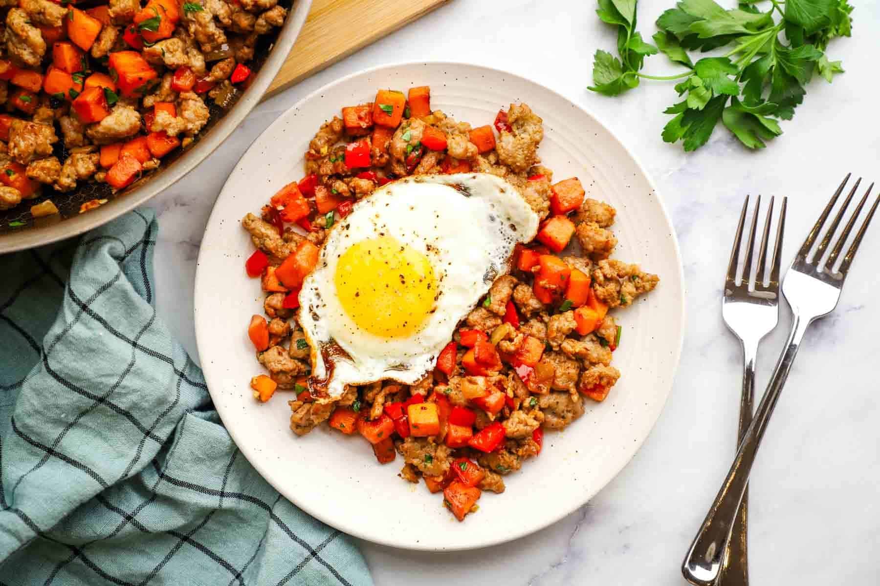 overhead view of a plate of sweet potato and sausage hash with a fried egg on top