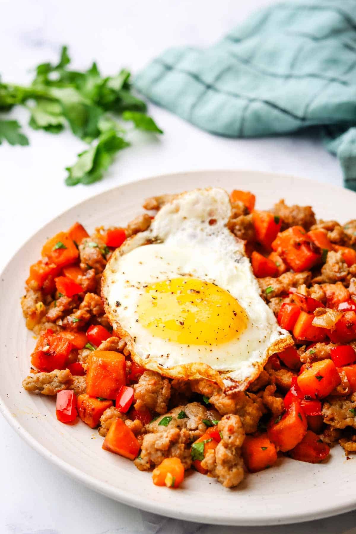 a plate of sweet potato and sausage hash with a fried egg on top
